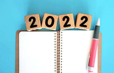 An open notebook with a pink pen on a blue background. The year 2022 blocks above the journal.
