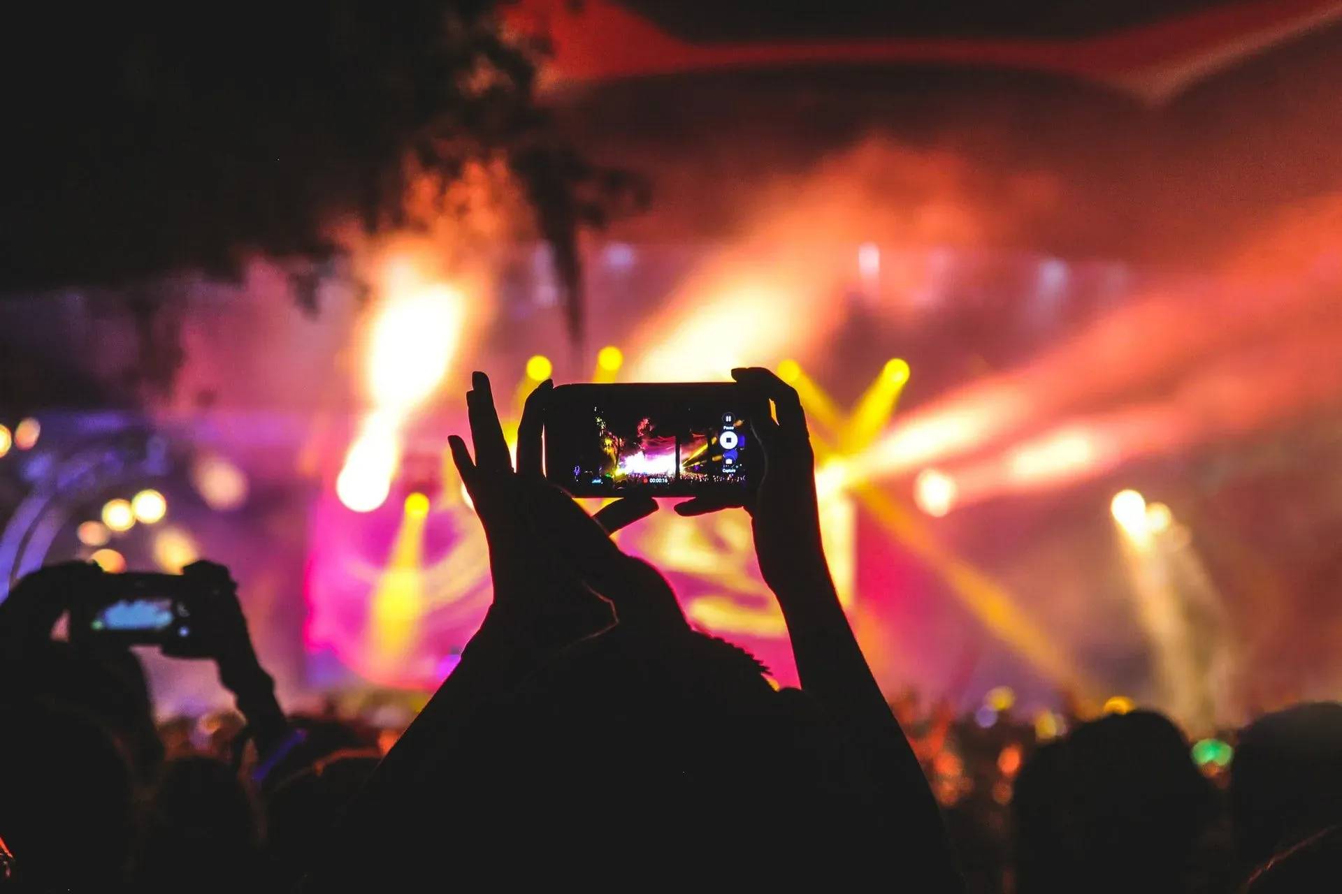  A person is holding a phone in their hand. The phone is being used to record a video of a concert. The stage is lit up with bright lights.